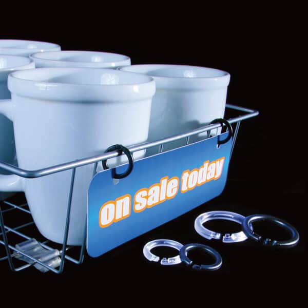 A wire display basket holding coffee mugs with a sale sign held in place with plastic rings.