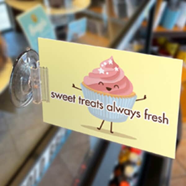 A suction cup with sign holder holds a small sign on a glass bakery display.