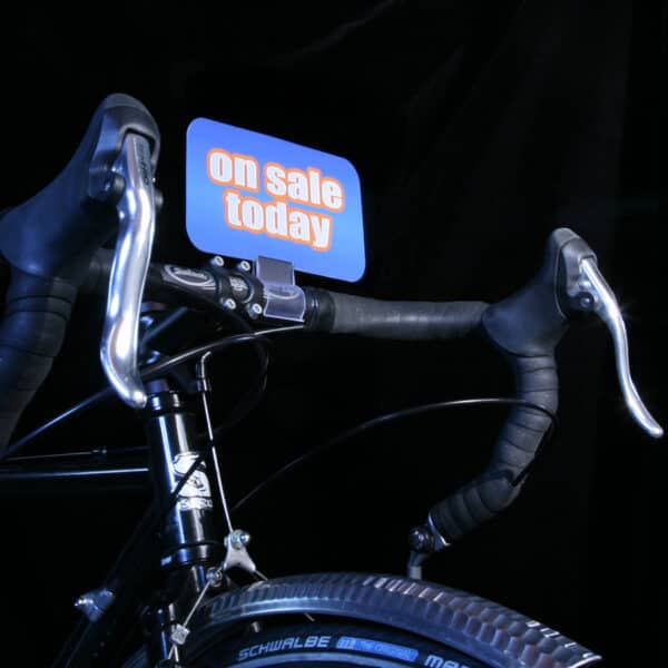 A small sign supported by a tube-grip sign holder attached to a bicycle handlebar.