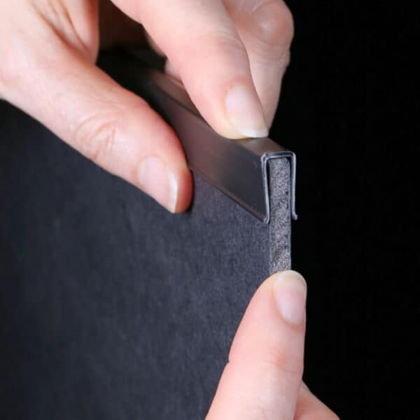 Popco foam board edge protector being placed on a piece of black foam board.