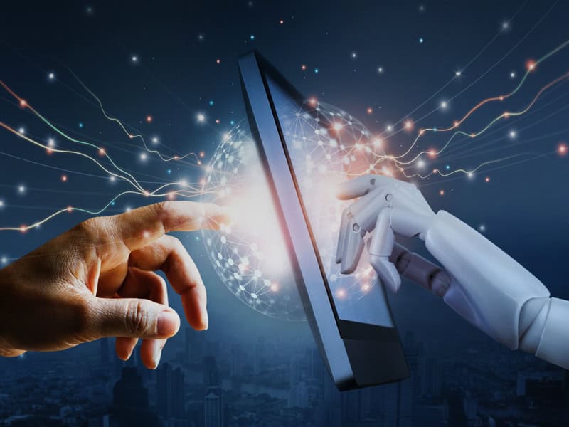 A digital image showing a human hand and a robot hand, each touching a computer monitor.